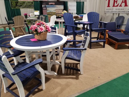 A display of outdoor furniture featuring a round table, colorful Adirondack chairs, and a flower arrangement.