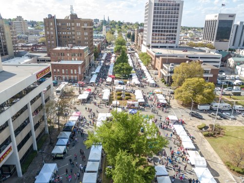 Aerial view of a bustling street market with numerous tents and crowds in a city setting.