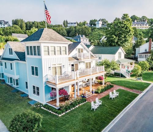 Aerial view of a blue house with a porch, surrounded by greenery and other homes, with an American flag flying.
