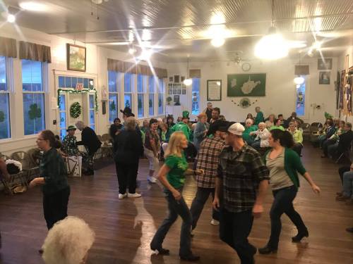 A lively gathering of people dancing in a decorated hall, celebrating with green attire and festive decorations.