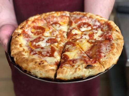 A person holding a freshly baked pepperoni pizza with melted cheese and a golden crust, sliced into wedges.