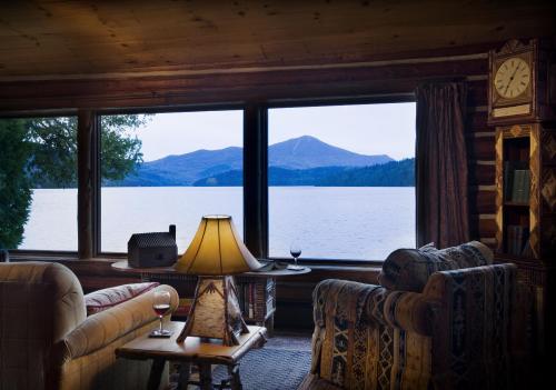 Cozy cabin interior with a view of a lake and mountains, featuring a lamp, wine glass, and comfortable seating.