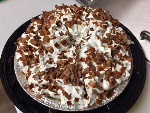 A chocolate pie topped with whipped cream and chocolate shavings, placed on a black serving tray.