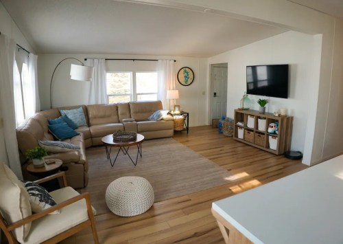 Cozy living room with a beige sectional, wooden furniture, a TV, and natural light from large windows.