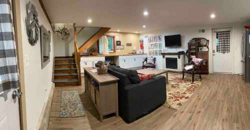 Cozy living room with a sofa, wooden stairs, and a fireplace, featuring warm lighting and rustic decor.