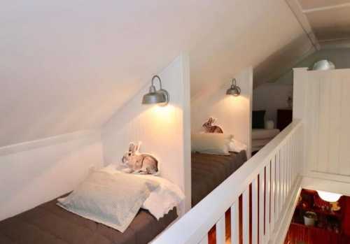 Two rabbits resting on beds in a cozy, sloped attic space with soft lighting and white walls.