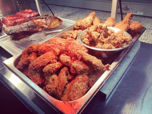 A tray of crispy fried chicken, with a side of barbecue ribs and additional fried pieces, all under warm lighting.