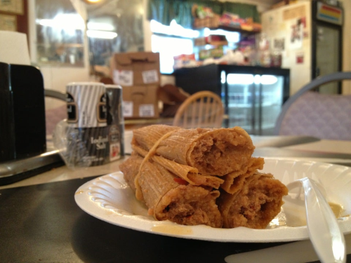 A plate of tamales stacked on a paper plate, with a casual dining setting in the background.