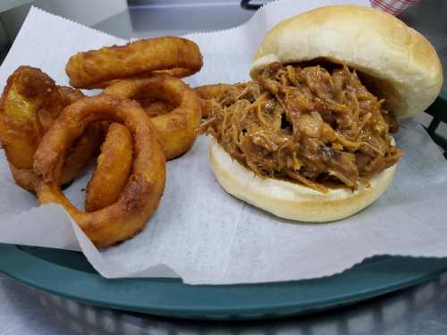 A pulled pork sandwich on a bun with onion rings on the side, served on a green tray with parchment paper.