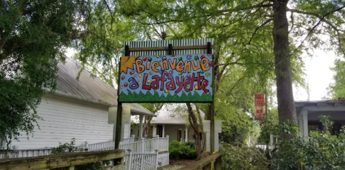 Colorful sign reading "Bienvenue à Lafayette" surrounded by trees and buildings.
