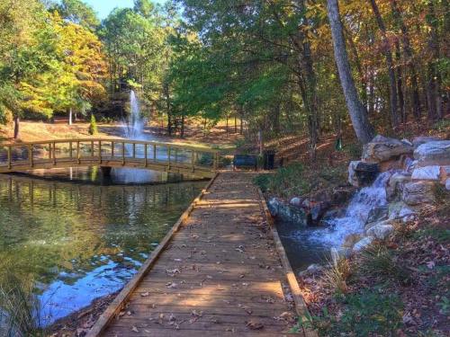 A wooden walkway leads to a pond with a waterfall, surrounded by trees and autumn foliage.