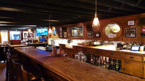 A cozy bar interior featuring a wooden counter, shelves of liquor, and warm lighting with framed photos on the walls.