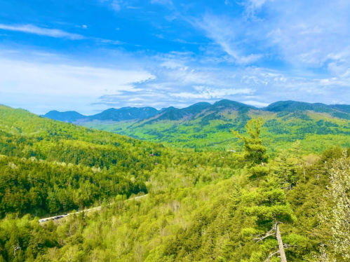 A panoramic view of lush green mountains under a bright blue sky with scattered clouds.
