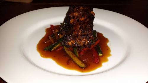 A beautifully plated piece of grilled fish atop sautéed vegetables, drizzled with a rich sauce.