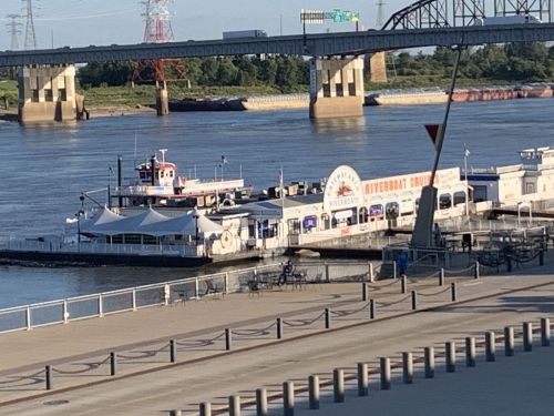 A riverboat docked at a waterfront with a bridge in the background and a clear blue sky.