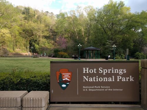 Sign for Hot Springs National Park with green trees and a gazebo in the background.