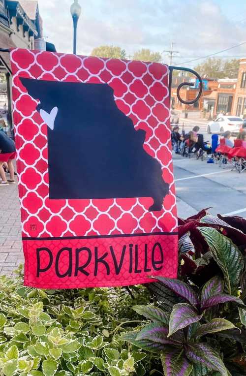 A decorative flag featuring a silhouette of Missouri with a heart, labeled "Parkville," against a red patterned background.