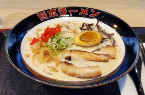 A bowl of creamy ramen topped with sliced pork, green onions, bamboo shoots, red peppers, and a soft-boiled egg.