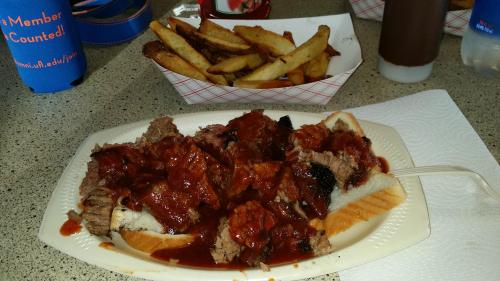 A plate of barbecue beef with sauce on a bun, served with a side of seasoned fries.