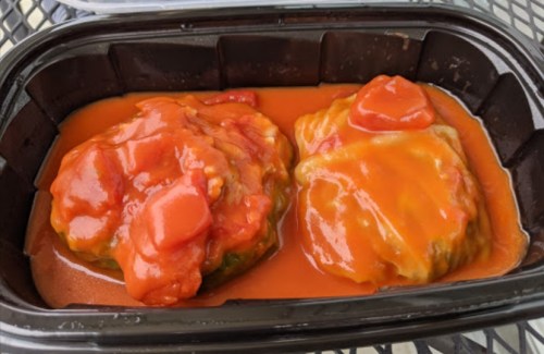 Two stuffed bell peppers in a black container, covered in a red tomato sauce.