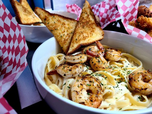 A bowl of fettuccine pasta topped with shrimp and garnished with parsley, accompanied by toasted bread triangles.