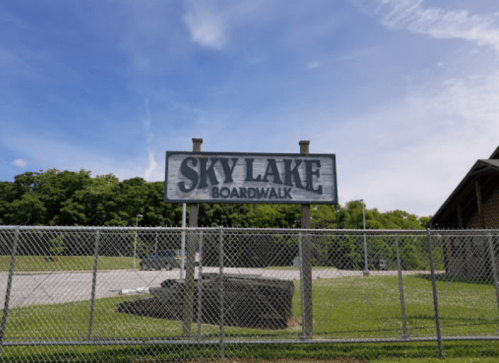 Sign for "Sky Lake Boardwalk" in front of a grassy area under a blue sky with scattered clouds.