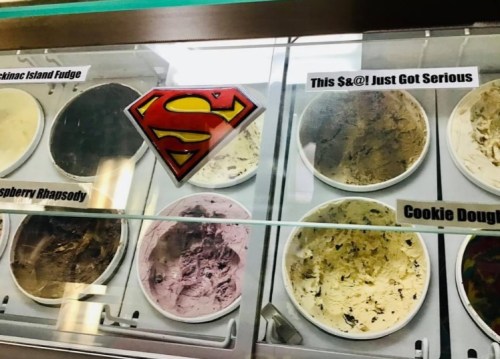 A display case of ice cream flavors with labels, including "Superman Fudge" and "Cookie Dough."