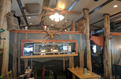 Cozy restaurant interior featuring wooden beams, antlers, and rustic decor with a mirror and tables.