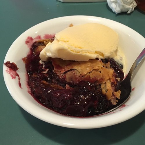 A bowl of warm berry cobbler topped with a scoop of vanilla ice cream.