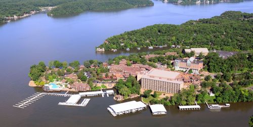 Aerial view of a lakeside resort with pools, docks, and lush greenery surrounding the water.