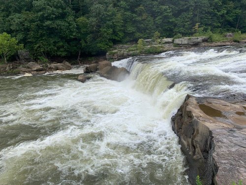 A waterfall cascading over rocky terrain, surrounded by lush green trees and a flowing river.