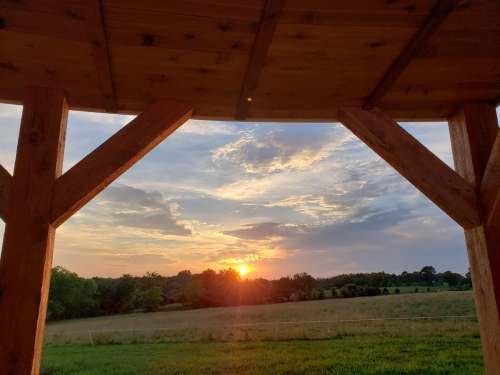 Sunset view through a wooden structure, with a colorful sky and green fields in the foreground.