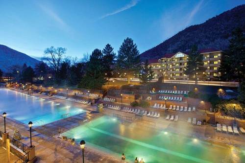 A serene outdoor pool area at dusk, surrounded by mountains and trees, with steam rising from the water.