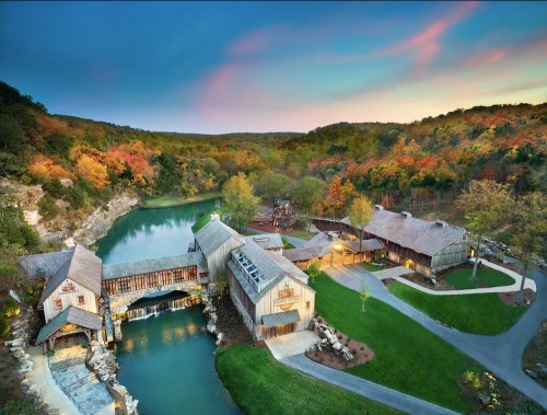 A scenic view of a rustic lodge by a tranquil lake, surrounded by colorful autumn foliage and rolling hills.