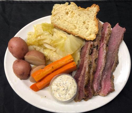 A plate with corned beef, cabbage, carrots, red potatoes, and a slice of bread, served with a mustard sauce.
