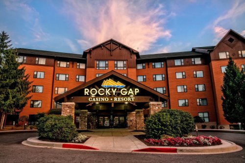 Exterior view of Rocky Gap Casino Resort, featuring a wooden facade and landscaped entrance under a colorful sky.