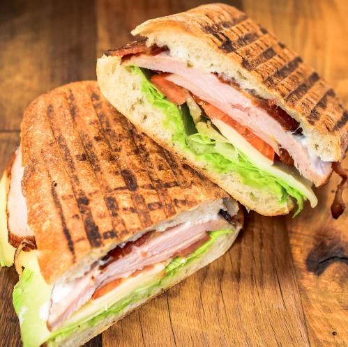 A grilled sandwich with layers of turkey, bacon, lettuce, and tomato, served on toasted bread.