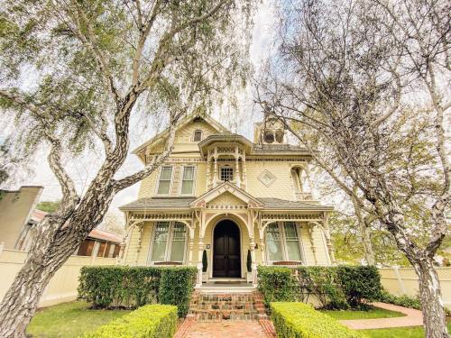 A charming Victorian-style house surrounded by trees and neatly trimmed hedges, featuring a grand entrance.