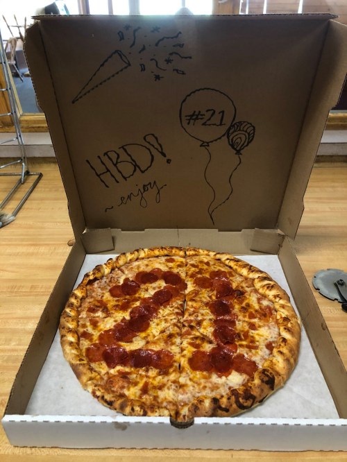 A pizza in a decorated box with "HBD! #21" written on it, featuring pepperoni slices and a festive design.