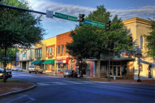 A street view of a small town intersection with shops, trees, and a traffic light at N. Court Square and Washington Street.