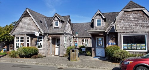 Charming wooden building with a shingled roof, featuring multiple windows and a welcoming entrance on a sunny day.