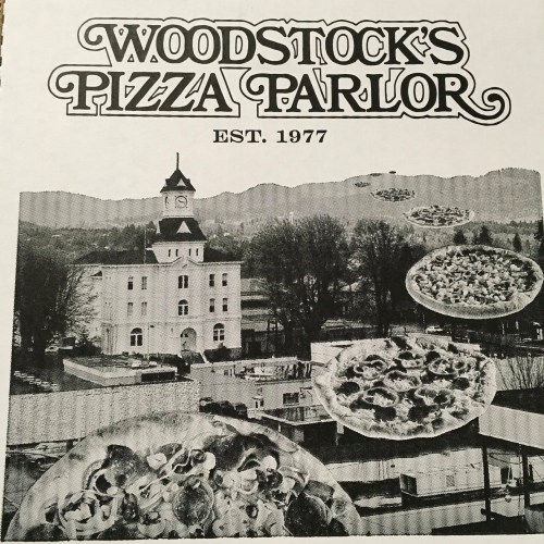 Black and white image of Woodstock's Pizza Parlor with floating pizzas and a historic building in the background.