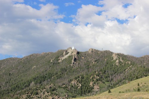 A mountainous landscape with rocky peaks and green forests under a partly cloudy sky.