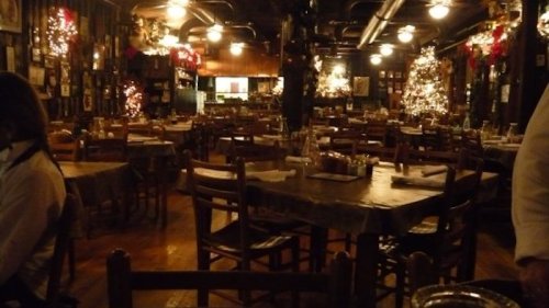 Cozy restaurant interior with wooden tables, chairs, and festive decorations, including Christmas trees and lights.