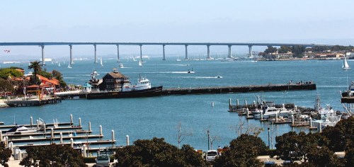 A scenic view of a harbor with boats, a bridge in the background, and a clear blue sky.