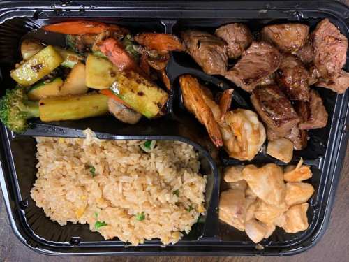 A takeout container with grilled vegetables, shrimp, beef, chicken, and fried rice.