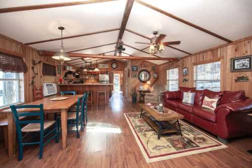 Cozy wooden interior of a home featuring a dining table, red sofa, and rustic decor with natural light.