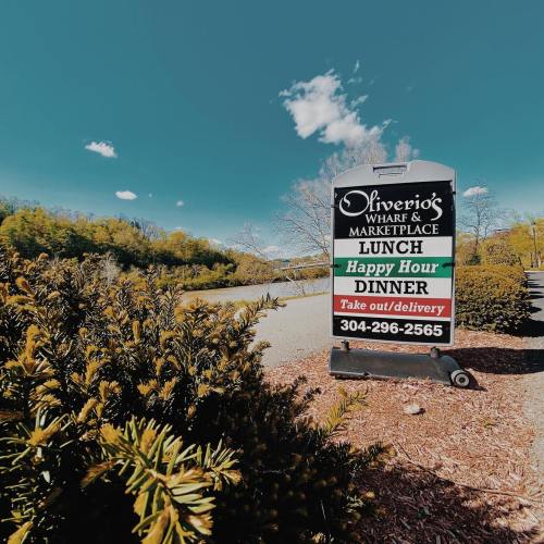 Sign for Oliverio's Wharf & Marketplace, listing lunch, happy hour, and dinner options with contact number.