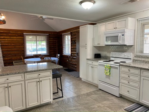 Bright kitchen with white cabinets, granite countertops, and a dining area featuring a wooden table and chairs.