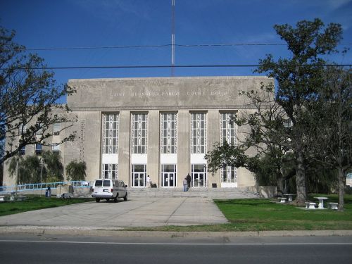 A large, modern courthouse with a symmetrical facade, tall windows, and trees in front under a clear blue sky.